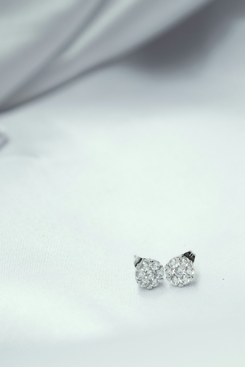 Two silver cluster earrings resting on white fabric.