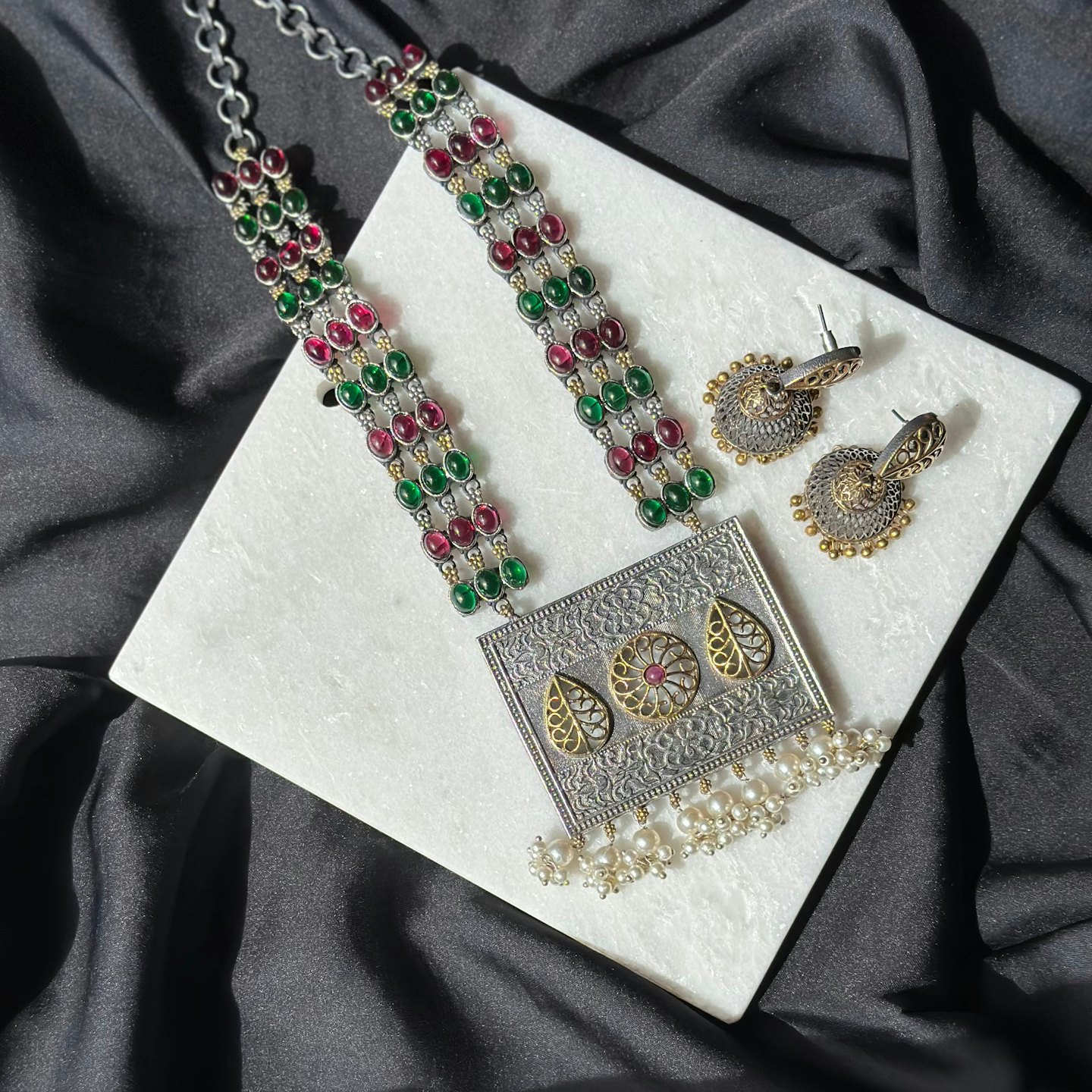 Ornate silver jewelry set displayed on a white marble slab.
