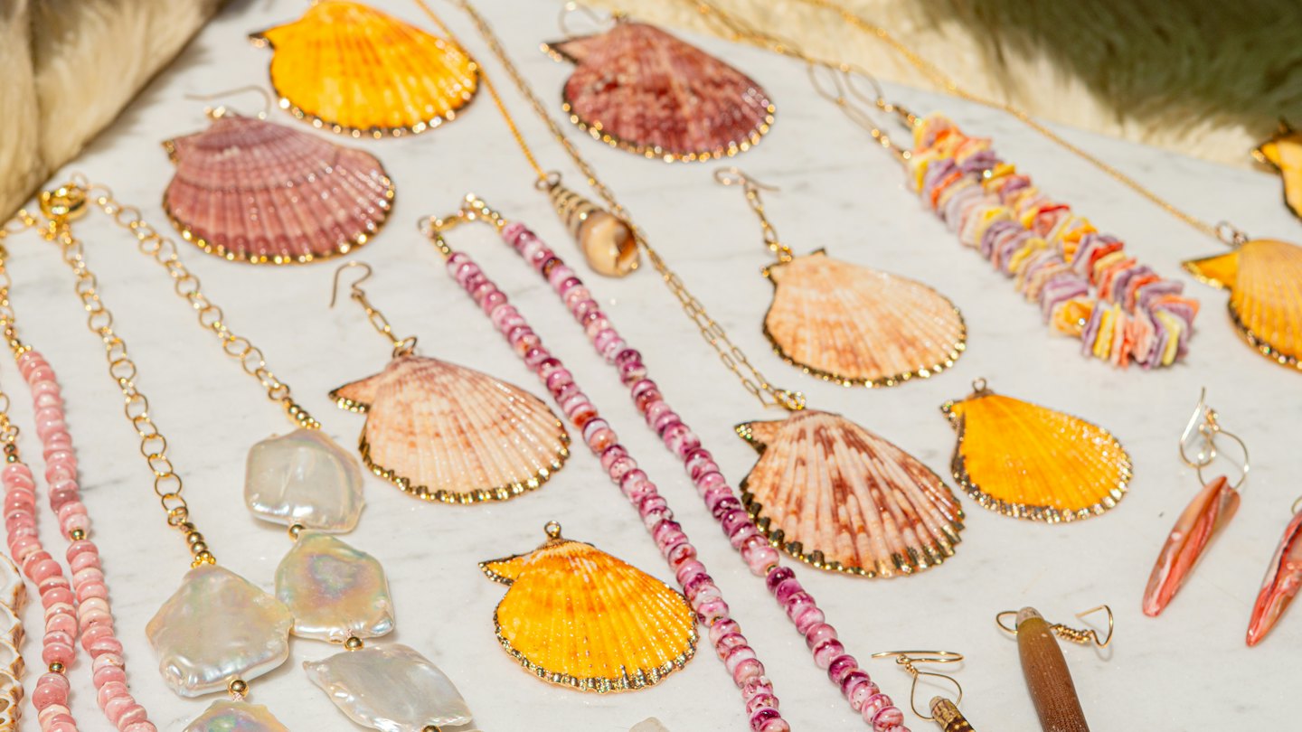 Handmade shell and pearl jewelry arranged on a marble surface.