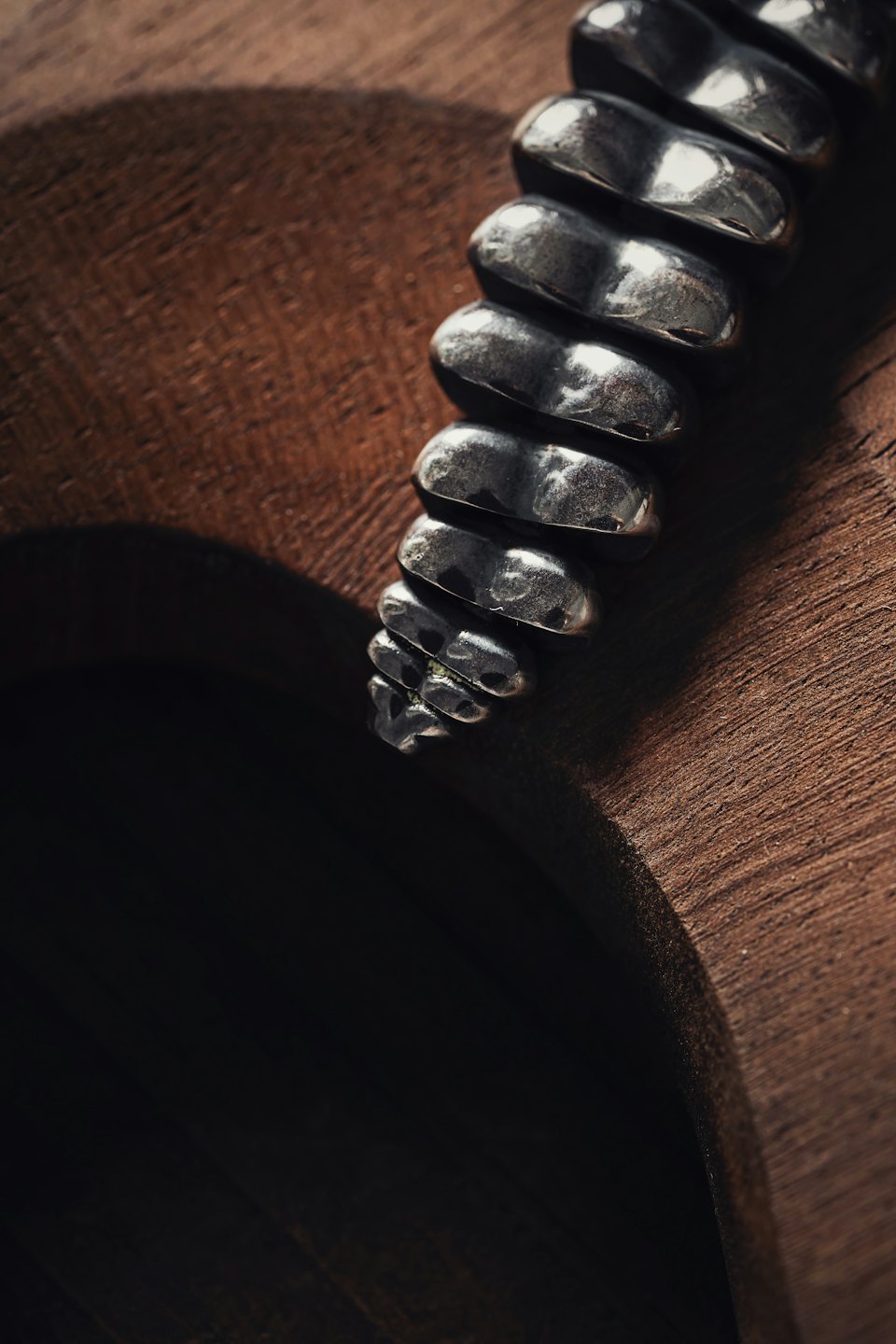A hammered silver bracelet rests on a wooden surface.